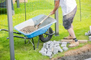Mannetje van Sunny Hoveniers in Lochem legt met een Kann-wielkar en Barenbrug-natuursteen een nieuwe bestrating aan in een tuinrenovatie.