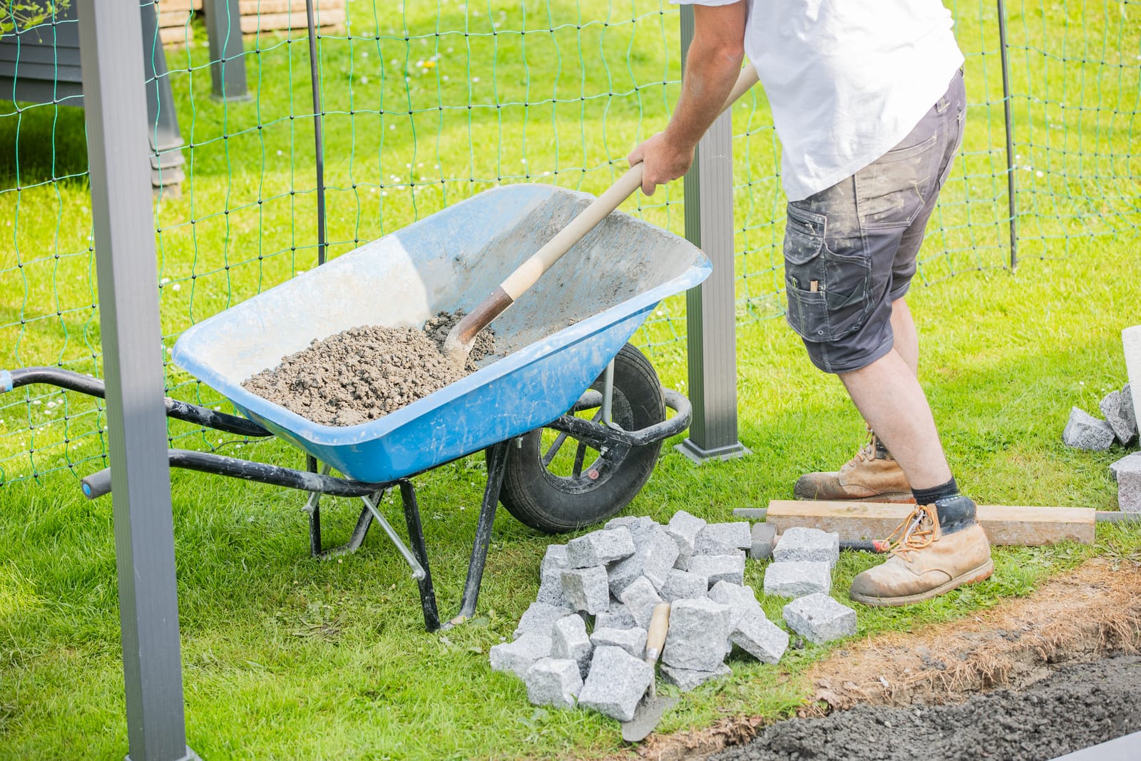 Mannetje van Sunny Hoveniers in Lochem legt met een Kann-wielkar en Barenbrug-natuursteen een nieuwe bestrating aan in een tuinrenovatie.